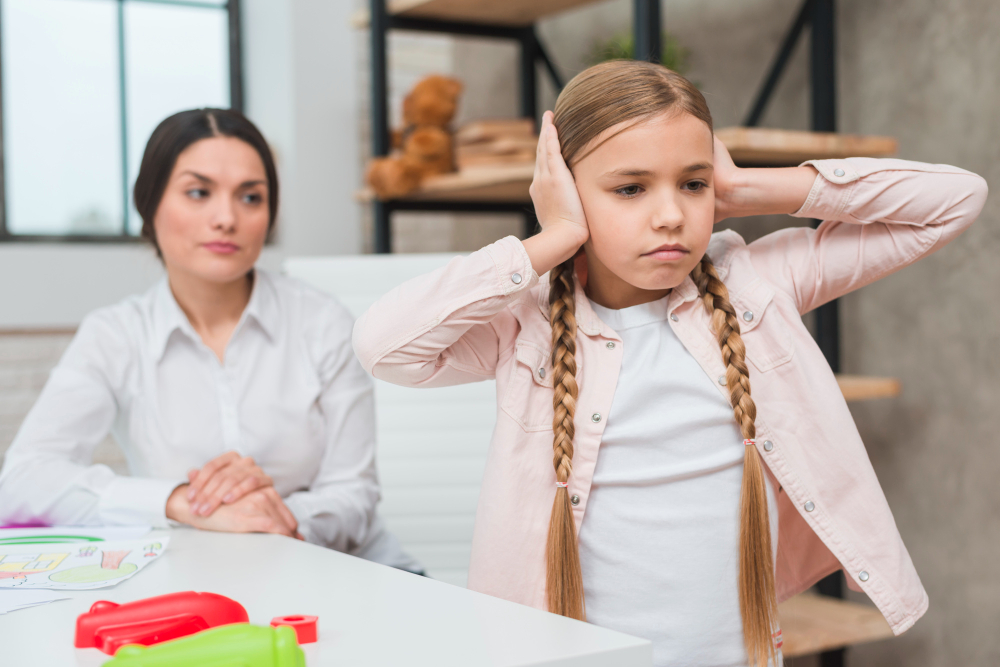 Close-up of female psychologist looking at annoyed girl covering her ears with two hands