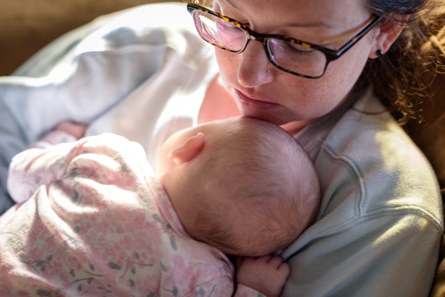 Woman with glasses sitting with a baby snuggled to her chest