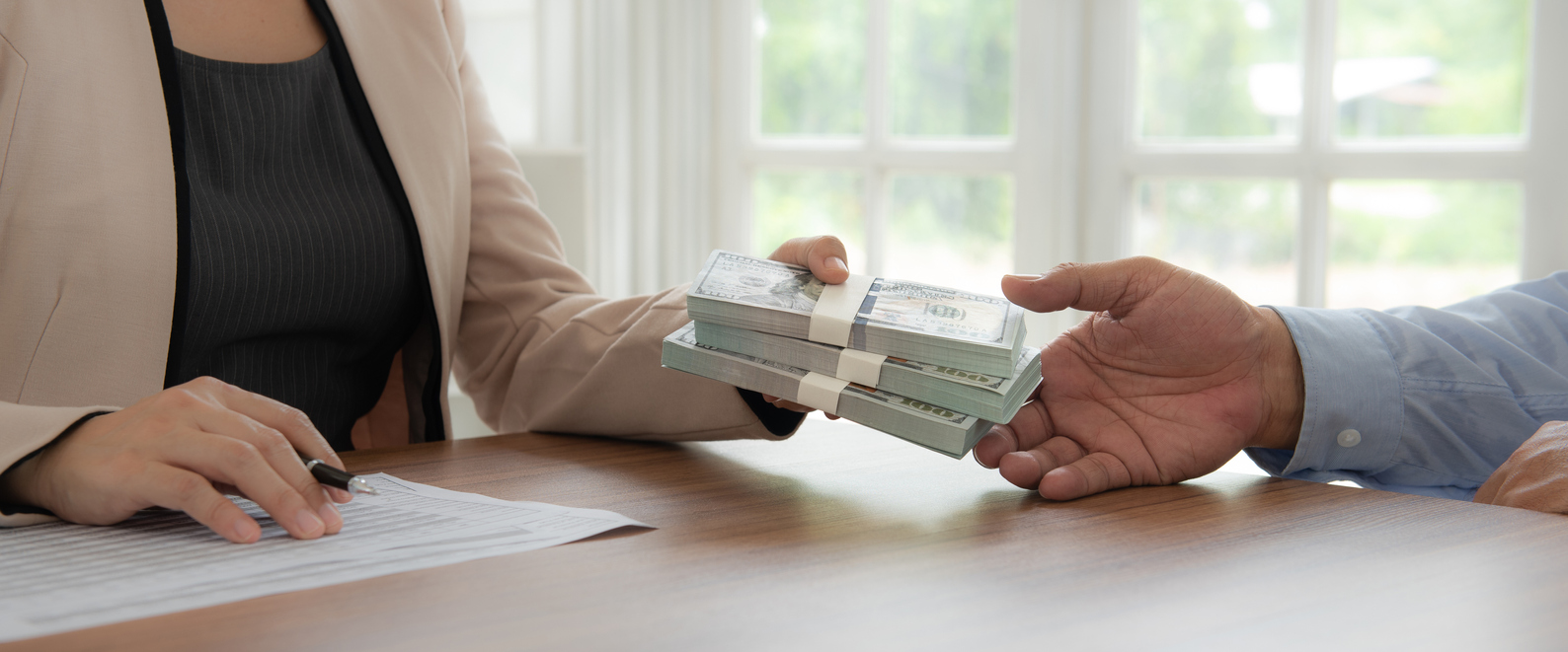 A woman handing money to a man at a desk, discussing their defenses in creditor lawsuits.