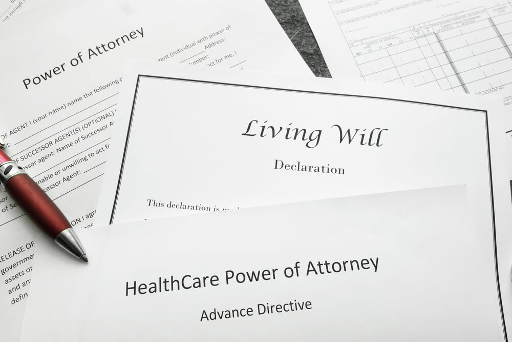 Different estate planning documents such as a power of attorney, living will, and a healthcare power of attorney laid out on a dest with a pen on top of the paperwork 