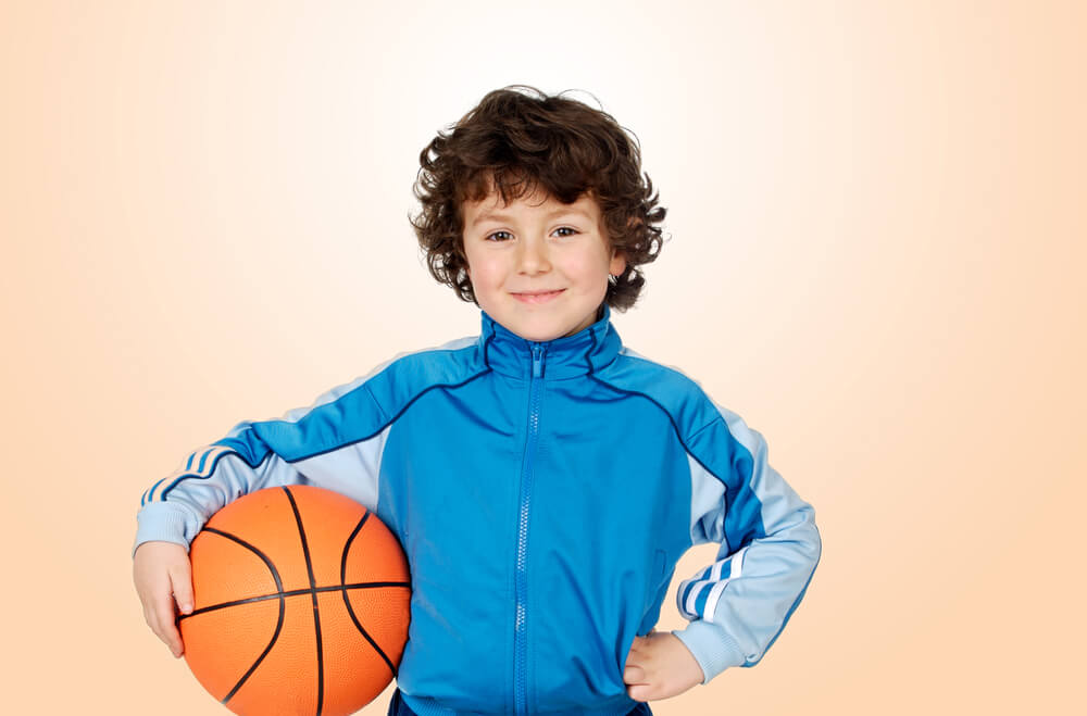 Little boy in a blue jacket holding a basketball with an orange background 