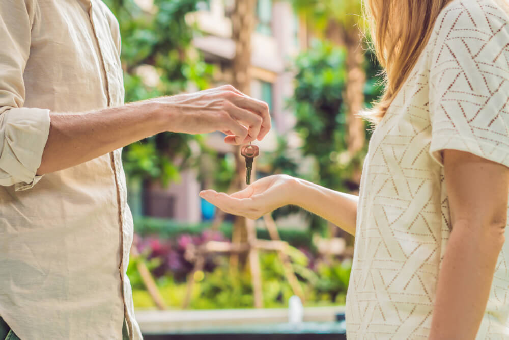 A close up of a man to the left giving keys to a women with plants behind them