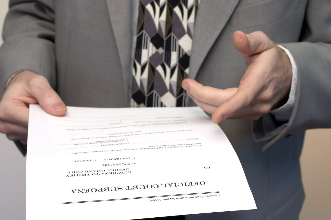 Man in grey suit holding an official court subpoena paper 