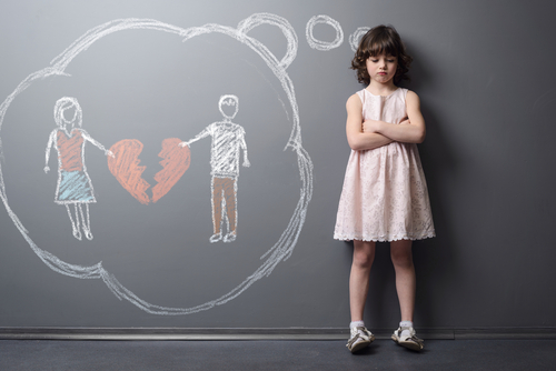 A young girl stands with crossed arms in front of a chalkboard displaying two figures holding a broken heart, symbolizing the emotional turmoil of a Texas custody battle.