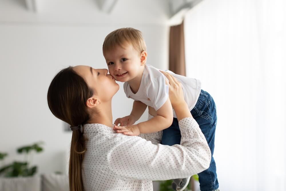 Mother holding her son in the air and kissing his check, the son is happy and smiling 