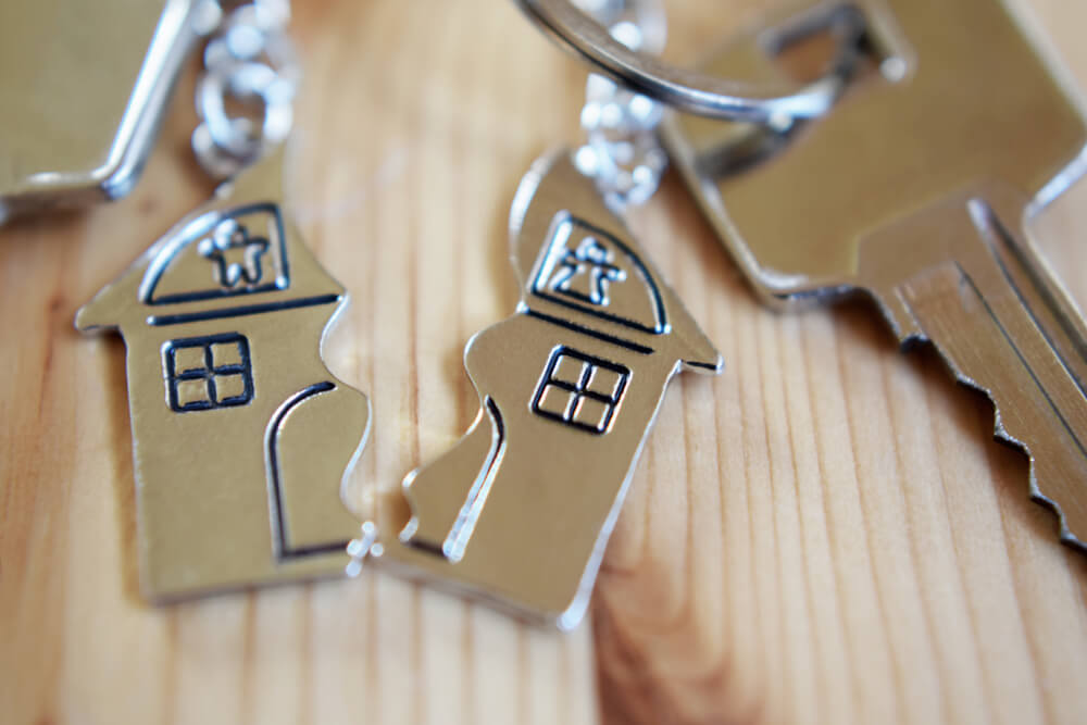 A sliver house keychain that is split in half, the right one is attached to a key on a wooden surface