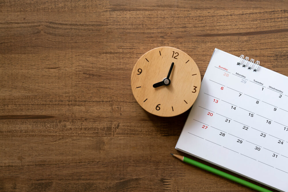 A calendar sitting on a wooden table next to a wooden clock