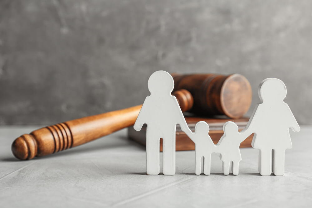 Paper cut out of a family with a judges mallet on a grey surface 