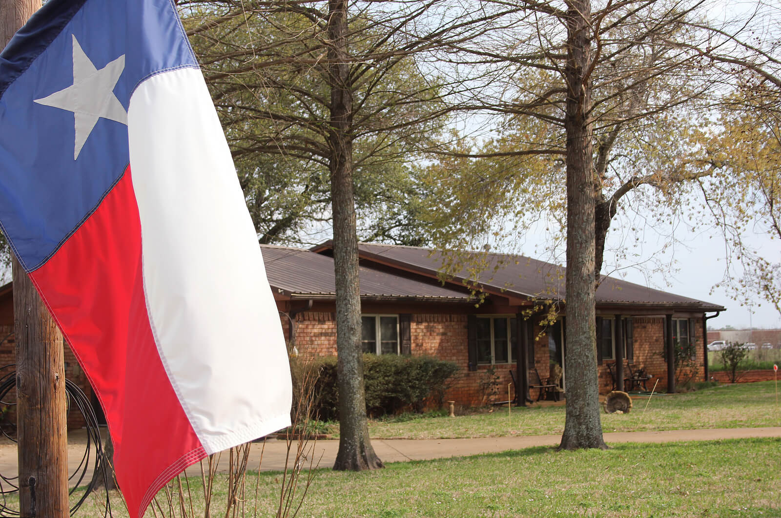 Texas flag with a single story brick home in the background