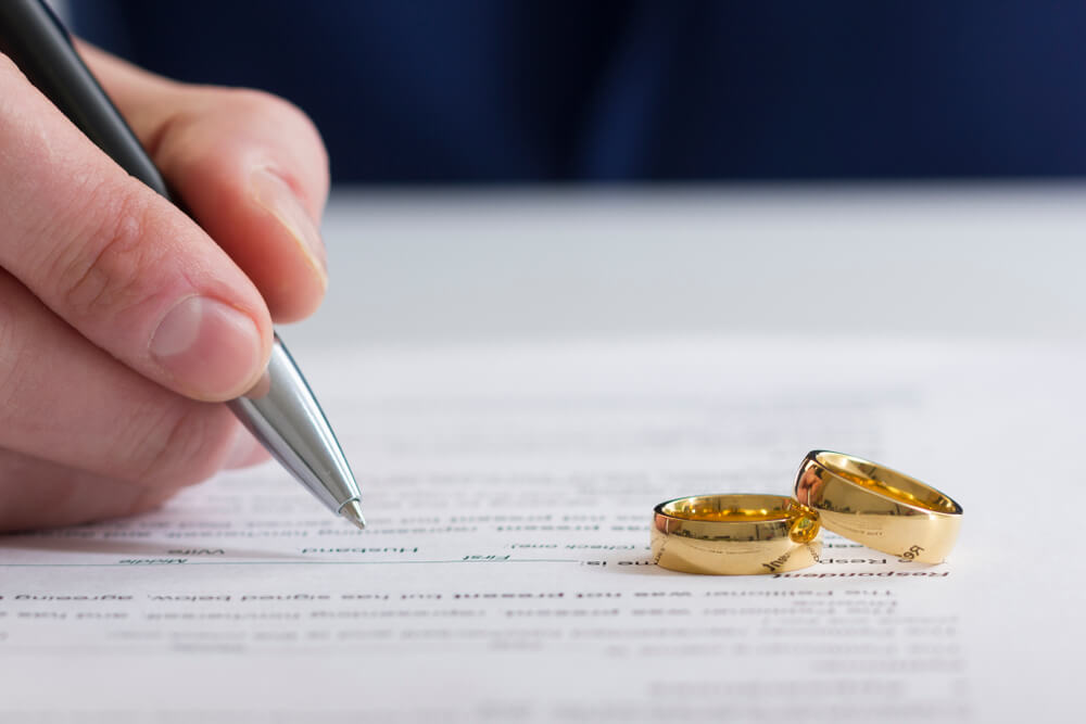 A document with two wedding rings on top of it and a person writing on the document 