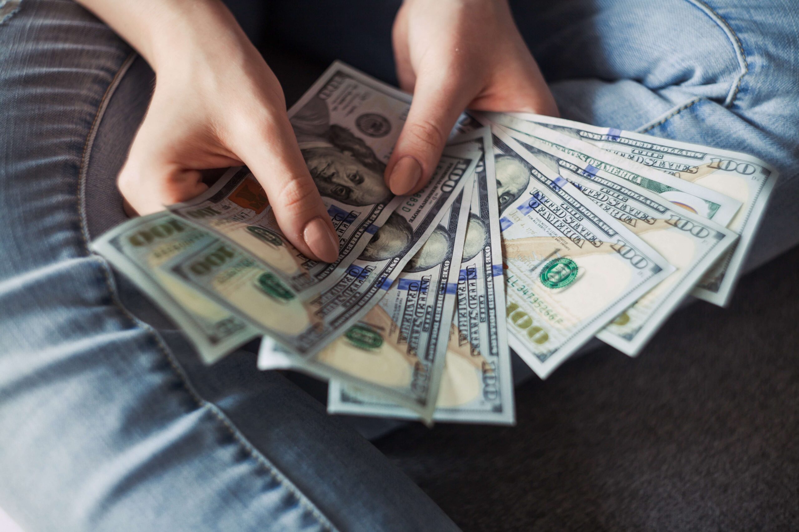 Person sitting on the ground counting $100 bills 