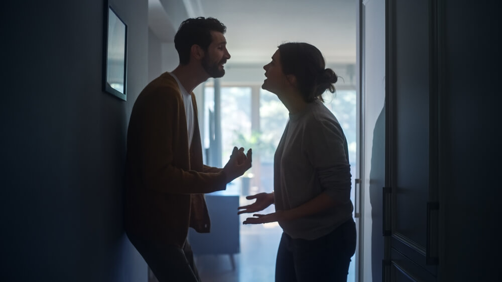 A couple standing in a dark hallway arguing 