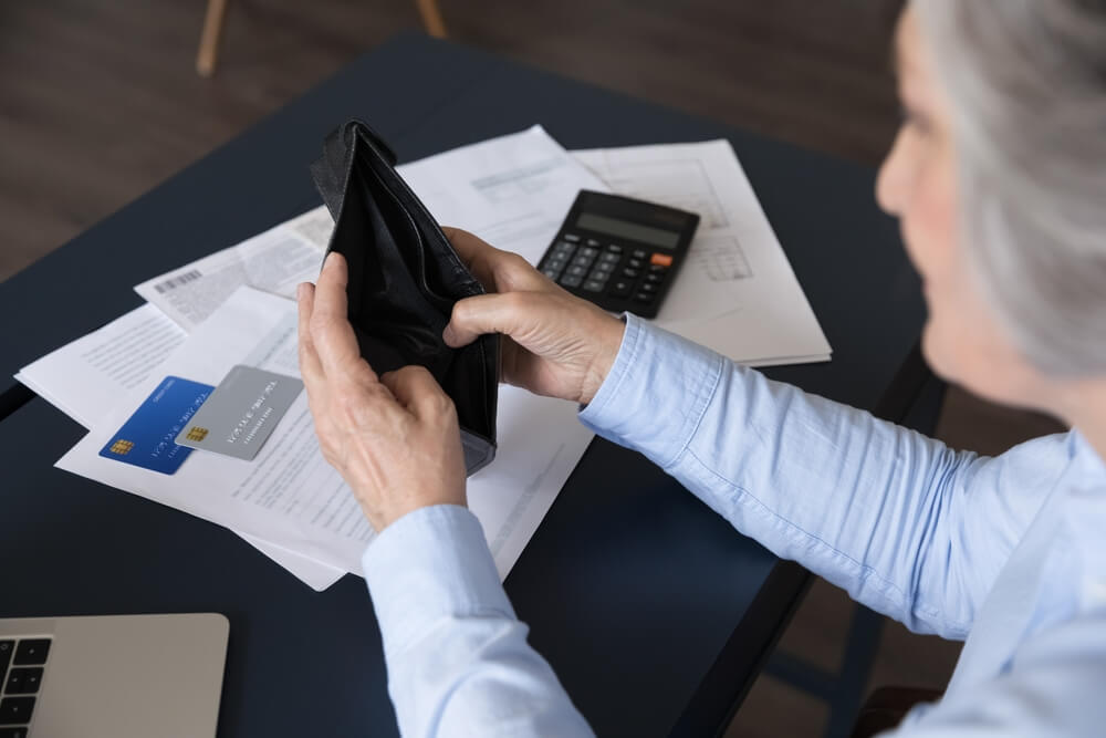 A woman sitting at a table with papers spread out and two credit cards on the papers, the woman opened her wallet but there is nothing inside