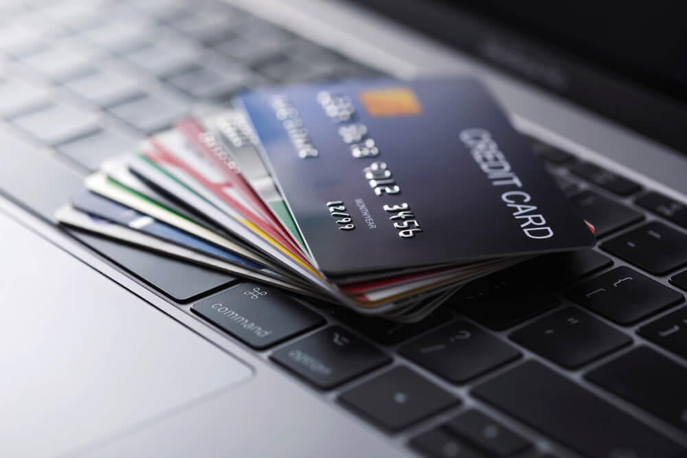A stack of many different credit cards fanned out while sitting on the keyboard of a laptop