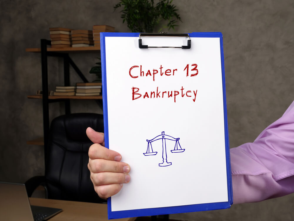Someone holding a chipboard with a paper that says chapter 13 bankruptcy in red with the scale of justice below it in blue 