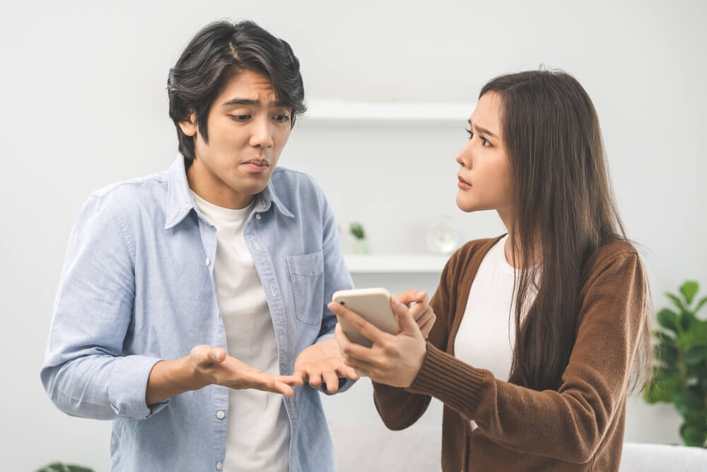 A woman looking at her husbands phone and looks angry while she shows the husband 