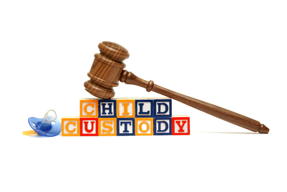 The word child custody spelling out in children playing blocks with a pacifier next to the blocks and a gavel on top of the blocks