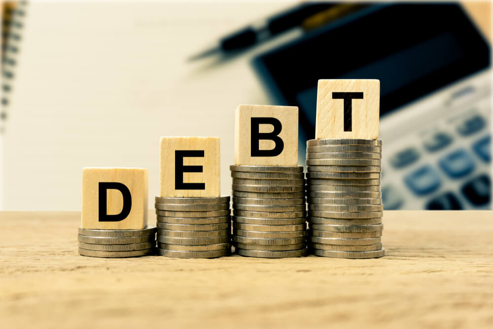 Wooden blocks spelling out the word debt on a stack of coins the increases as the word is spelled 