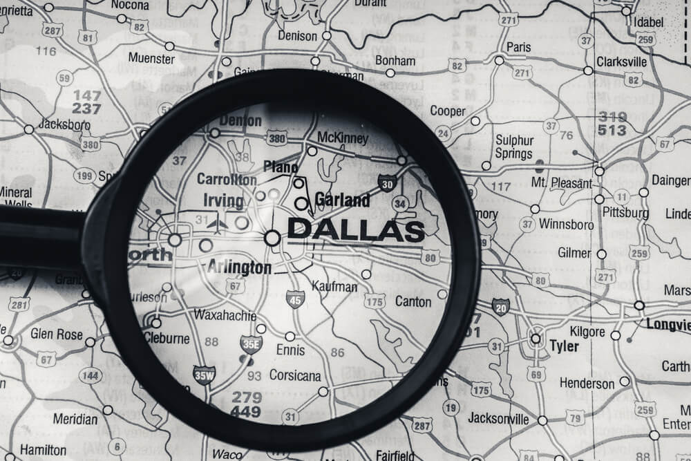 A black and white map of north Texas with a magnifying glass over the city of Dallas