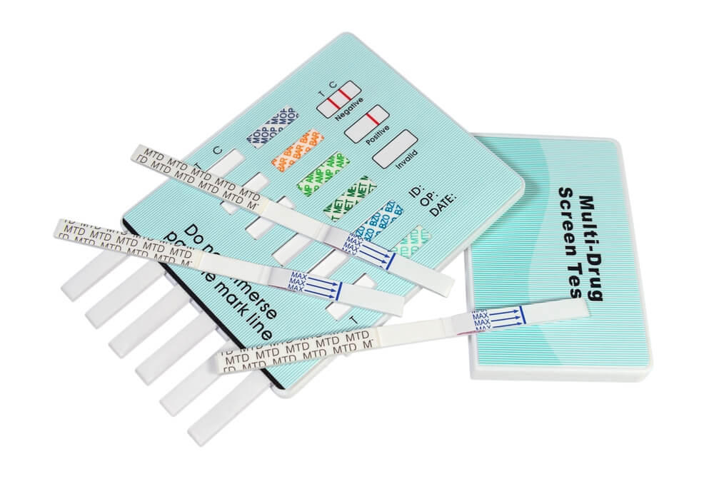 A multi drug screen test laying on a white surface and on top of the drug screening set there are three one step methadone strips