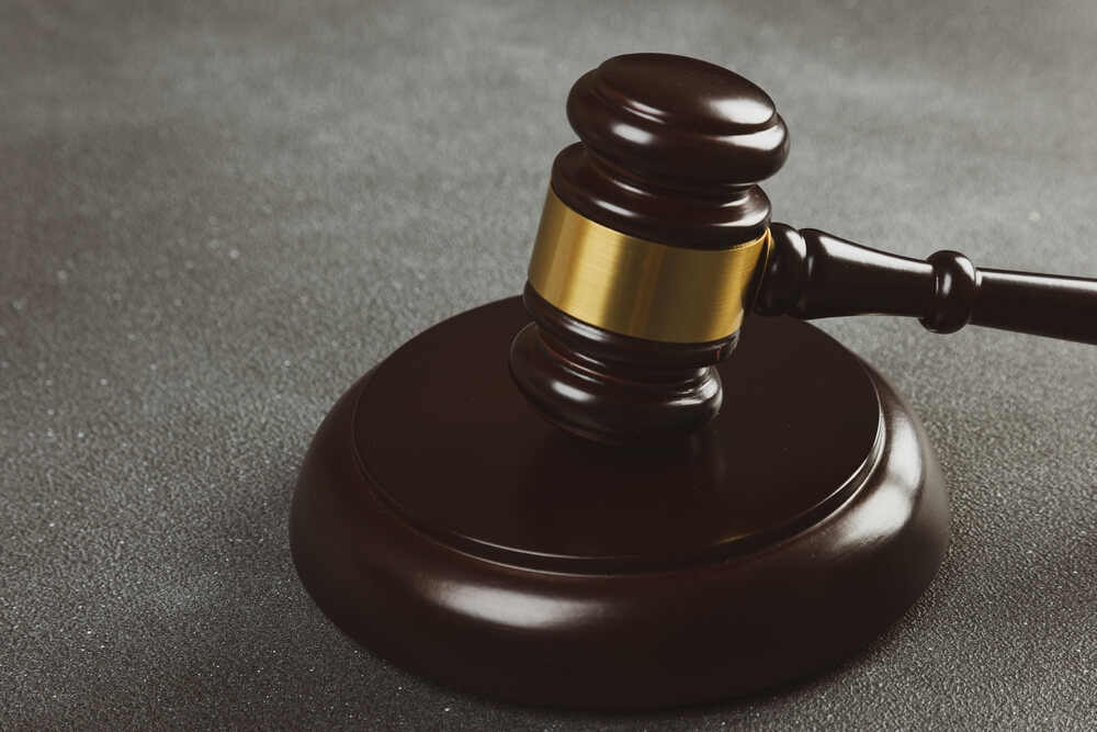 A close up of a judge's gavel hitting the sound block on a grey surface