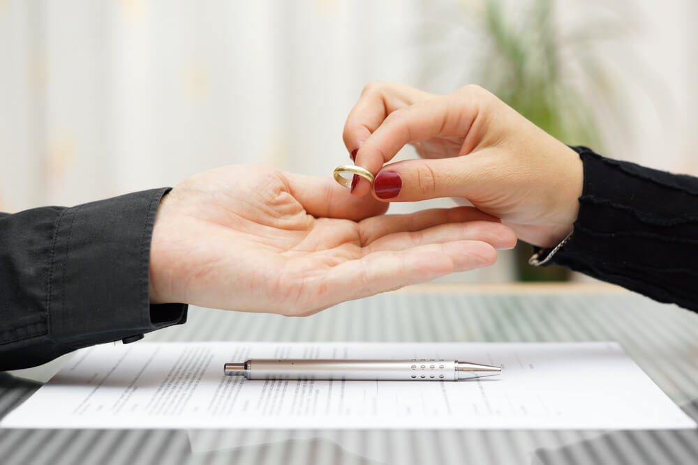 A women returning her wedding ring to her newly ex husband with divorce papers below their hands