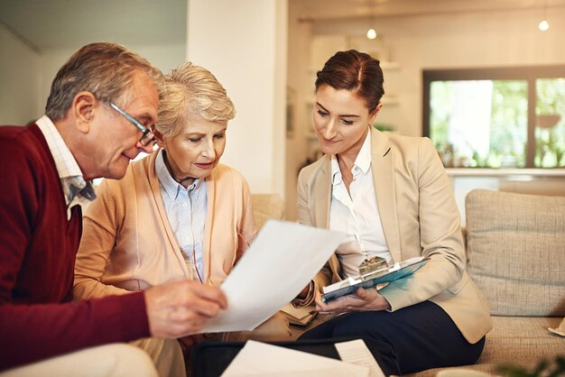 An older couple reviews documents with a professional woman on a couch in a cozy living room setting.