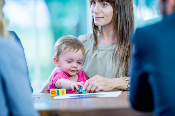 A woman holds a baby seated at a table, where the baby is playing with colored blocks and paper. It's moments like these that remind us of the importance of nurturing family bonds, as co-parenting effectively can be crucial in maintaining custody and providing stability for your child's growth.