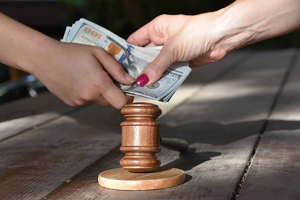 Two hands exchanging a stack of dollar bills over a wooden gavel placed on a wooden surface subtly illustrates why divorce is so expensive.