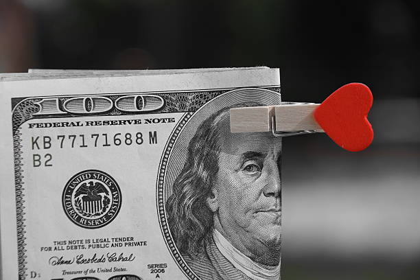 A 100-dollar bill is clipped with a wooden peg, adorned with a red heart shape on one end, symbolizing the love and support akin to learning how to get spousal support in Texas.