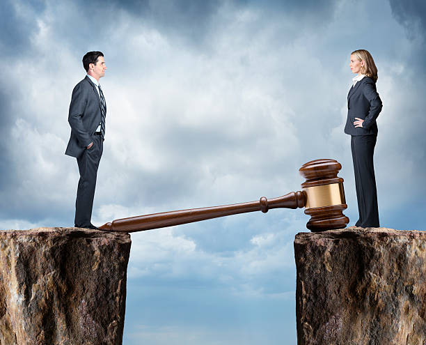 A man and woman in business attire stand on opposite cliffs, the large gavel bridging the gap under a cloudy sky, symbolizing the weighty decisions of how to get spousal support in Texas.