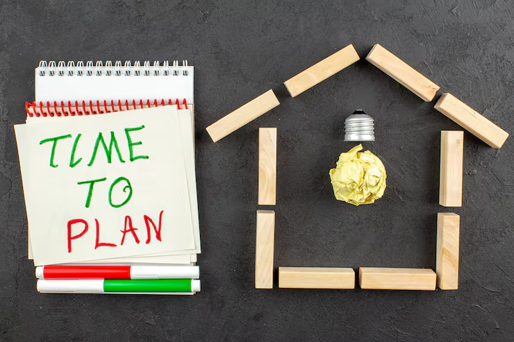 A notepad with "TIME TO PLAN" written in green and red marker sits beside wooden blocks forming a house shape, topped with a crumpled paper and light bulb—perfect symbols for brainstorming your trust-based estate plan.