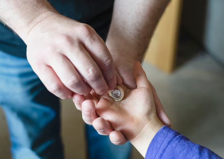 An adult hand places a coin into a child's open palm, symbolizing financial care and the process of how child support is calculated in Texas.