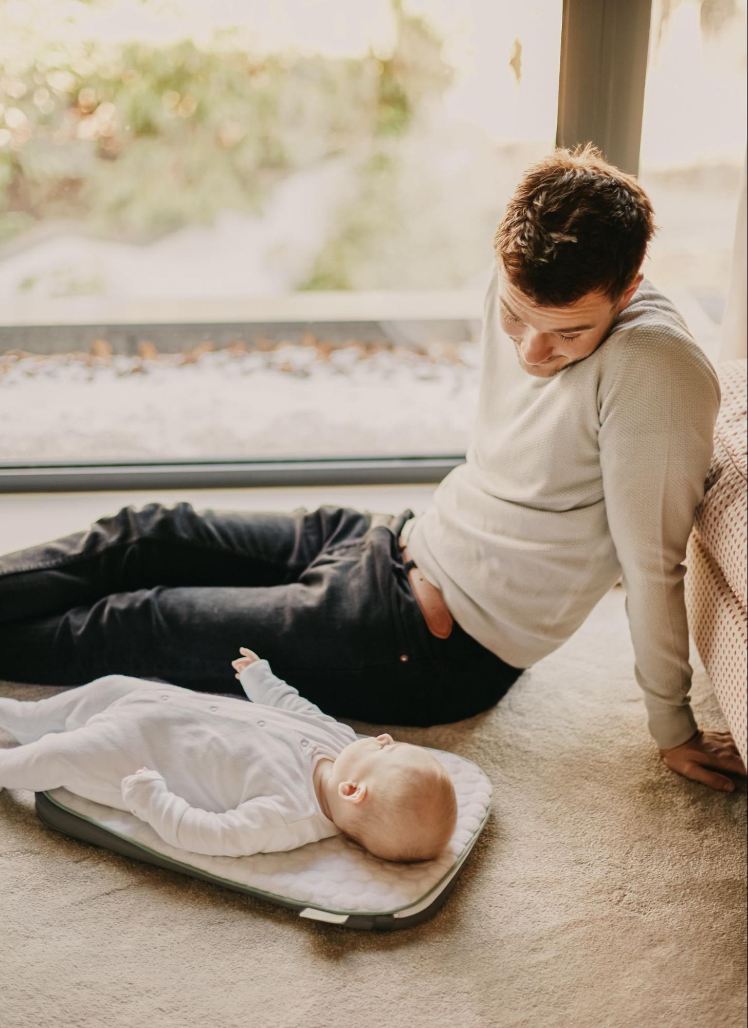 A man gently cradling a baby on a mat on the floor.