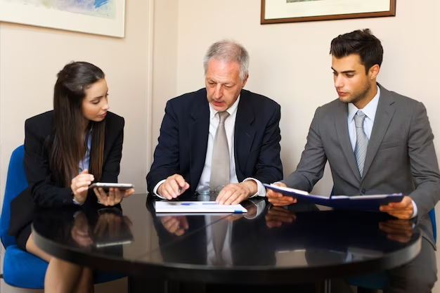 Three business people, sitting at a table in an office.
