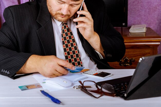 A man in a suit is talking on the phone while sitting at his desk, possibly discussing a situation concerning debt collectors and legal actions.