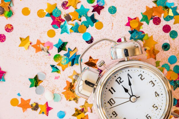 Alarm clock with confetti on a pink background.