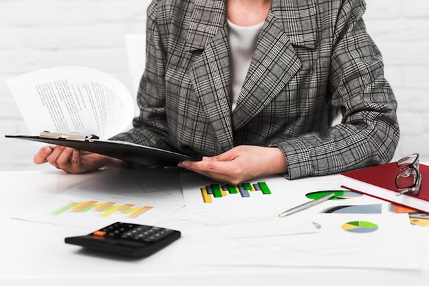 A business woman sitting at a desk with papers and a clipboard.