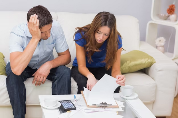 A man and woman sitting on a couch looking at papers.