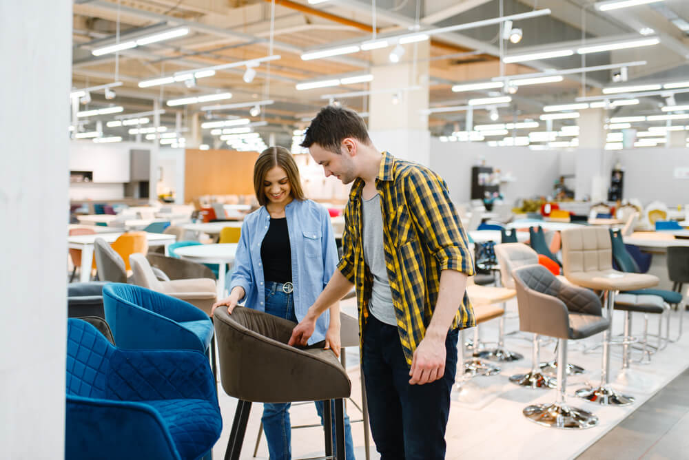 Man and woman walking around a furniture store but stopped to look at a grey chair