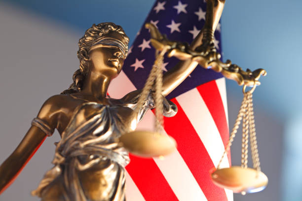 A statue of the Lady Justice stands in front of an American flag.