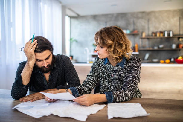 Young couple sitting at dining room at table, looking at divorce papers. man holding head with hand