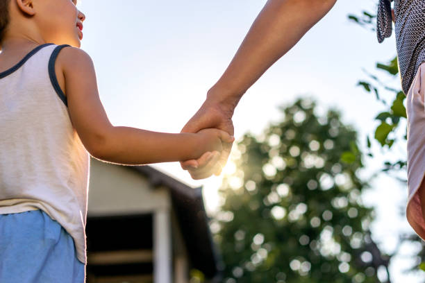 Mom and son holding hands in nature. Close up of mother and her son holding hands at the sunset. Mother and son holding hands walking at sunset. Parenting and family lifestyle concept. Copy space.