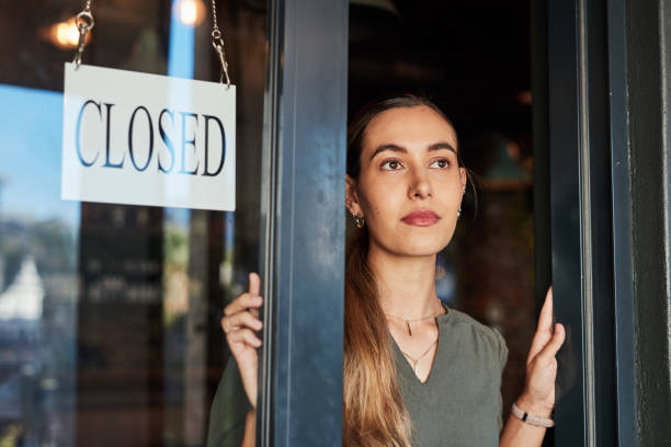Closed shop sign, woman thinking and female business owner at a cafe or restaurant. Young person, entrepreneur and employee closing coffee place with poster and bulletin of bankruptcy from debt commercial bankruptcy filings increase