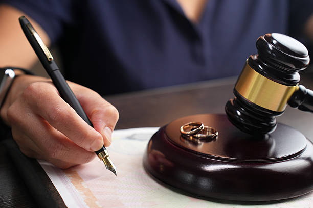 Close-up of a woman signing a divorce document next to a gavel and wedding ring in the background