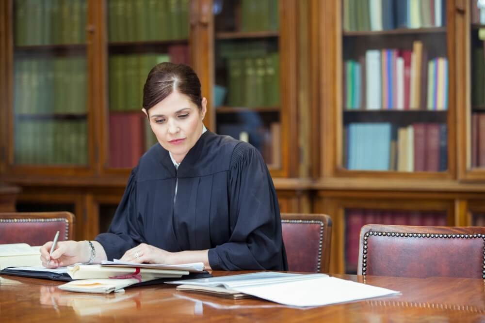 Female judge looking over a desk full of paperwork while writing in a notebook