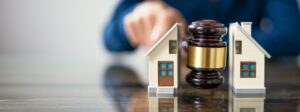 A toy house sitting on a table and a judge is hold his gavel splitting the house in two