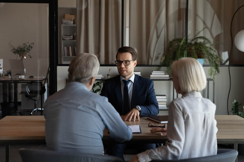 An older couple sitting at a desk in front of an attorney that is explaining something to the couple