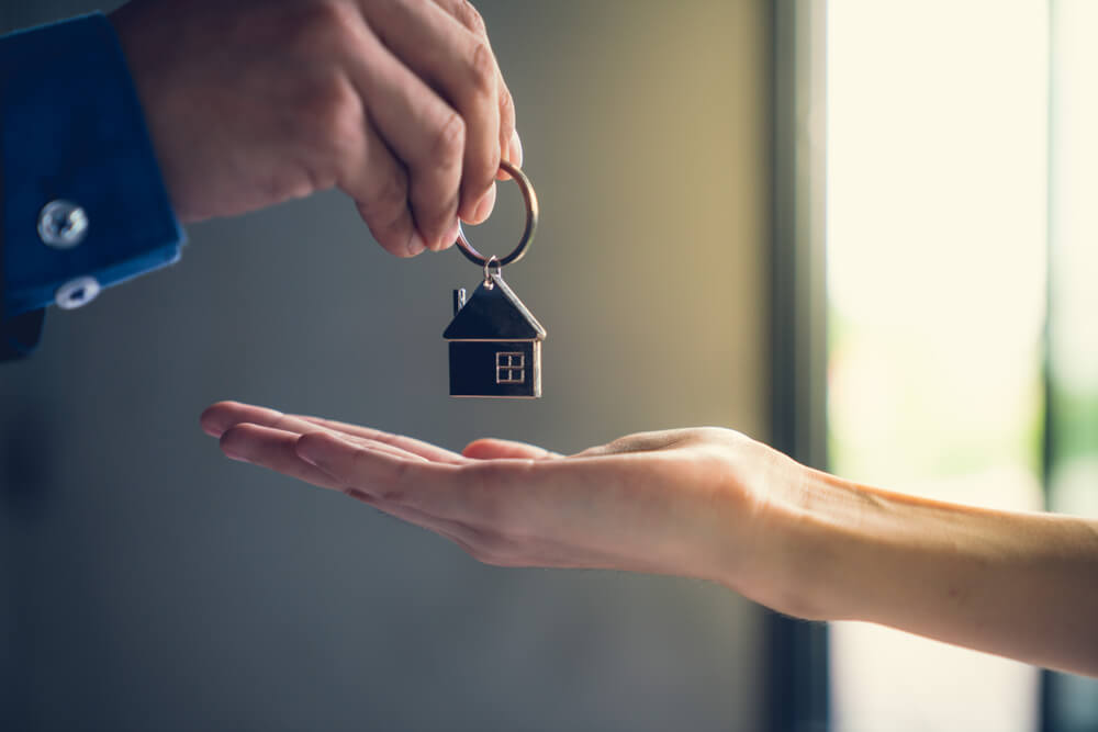 Someone holding out their hand with another person handing over a little house key chain