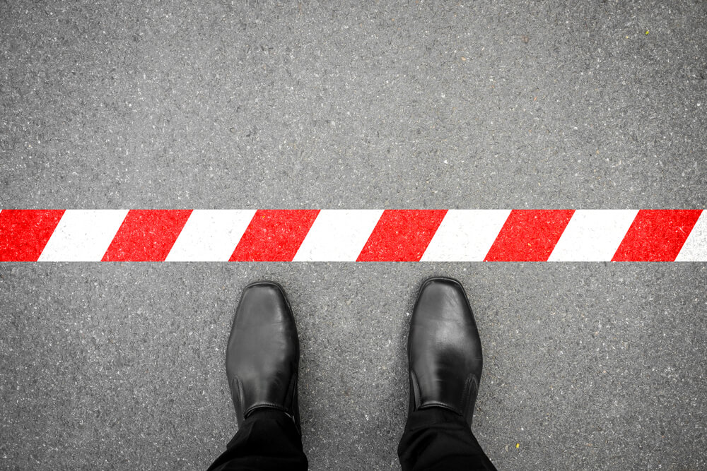 Black shoes standing on concrete with a red and white line in front of them